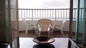 Varanda com mesa, duas cadeiras, guarda-corpo de vidro e vista do céu.