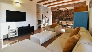 A modern living room with a flat-screen TV, a stone fireplace, a blue refrigerator, and a staircase leading to a dining area.