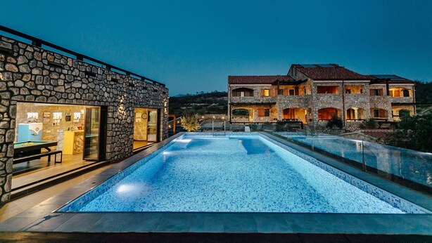 A swimming pool with stone walls and a large house in the background.