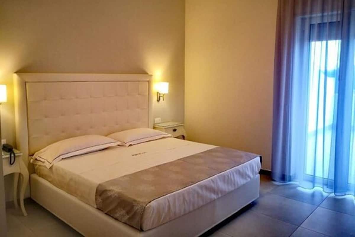 Una habitación de hotel con una cama grande, dos mesitas de noche y una ventana con cortinas.