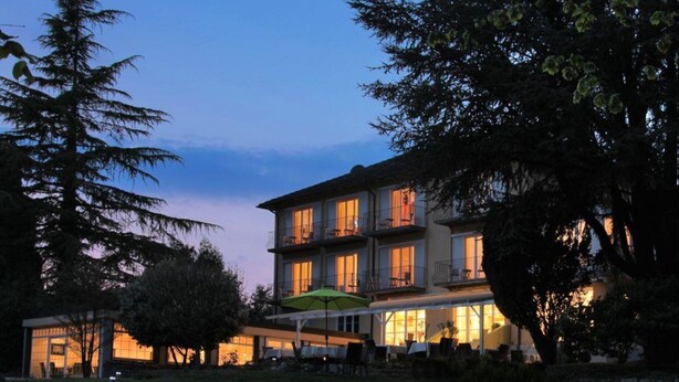 A multi-story building with balconies, a covered outdoor seating area, and a well-lit facade. - Hotel Lindenallee (Lindau)