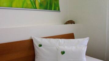 Una cama con ropa blanca y dos almohadas, una con diseño de hoja verde.