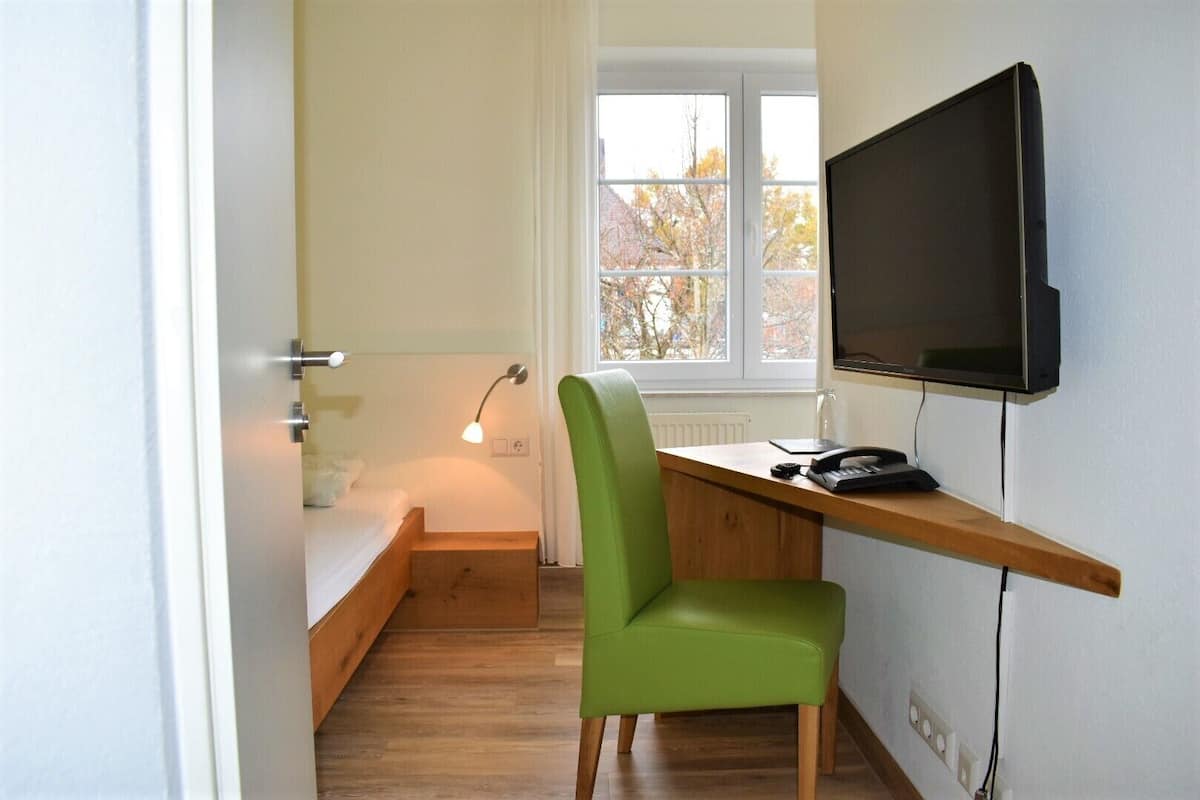 A small room with a bed, a desk with a chair, a TV, and a window with a view of trees.