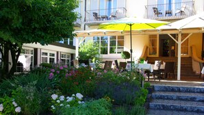 A hotel patio with outdoor seating, a garden with various plants, and a staircase leading to the entrance. - Hotel Lindenallee (Lindau)