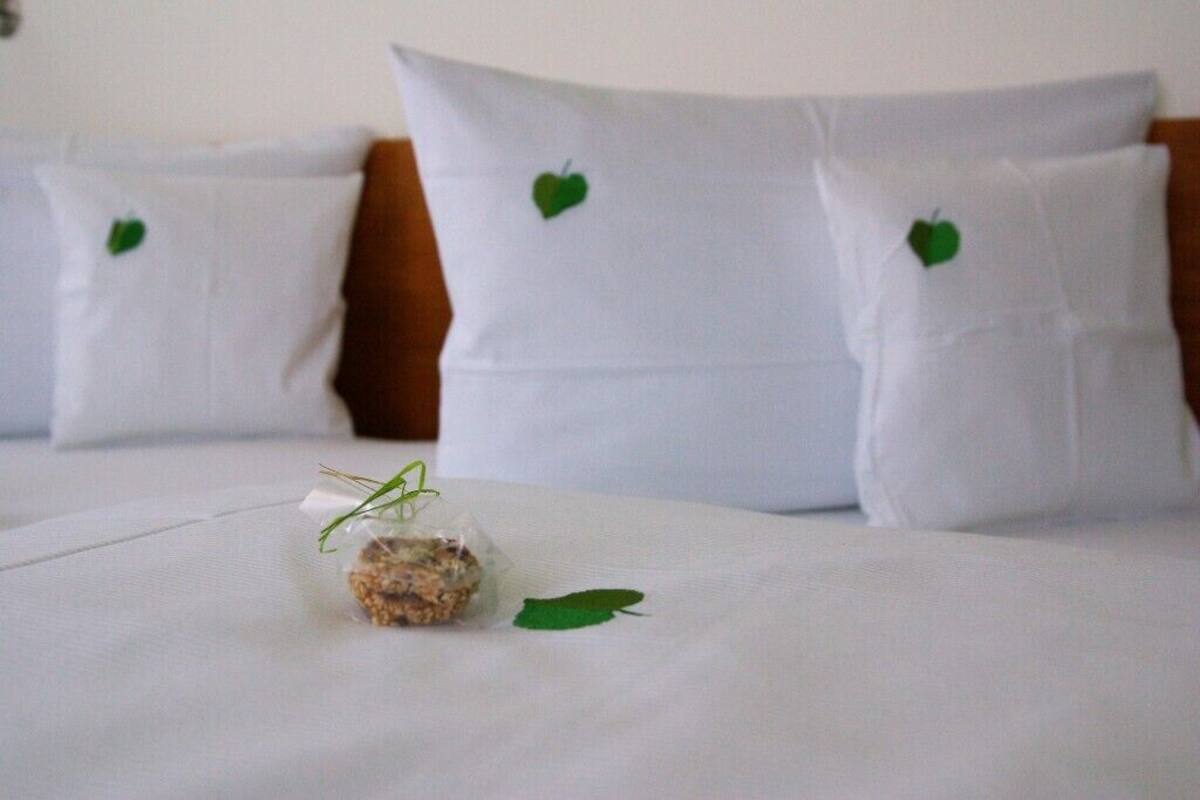 A neatly made bed with white bedding and pillows, each featuring a small green leaf design.