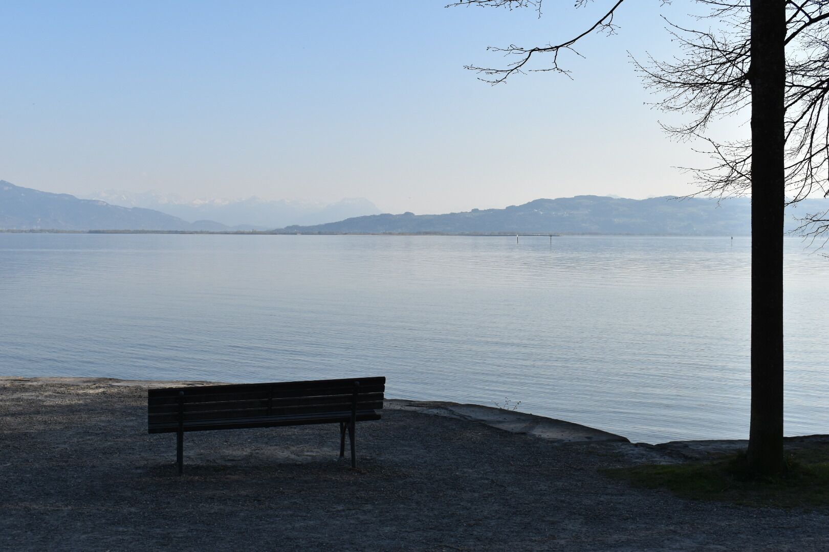 A bench by a calm lake with mountains in the background.