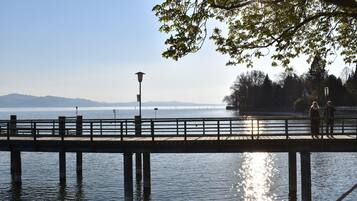 Eine Holzstege erstreckt sich in ruhiges Wasser, bewölkter Himmel und ferne Berge im Hintergrund.
