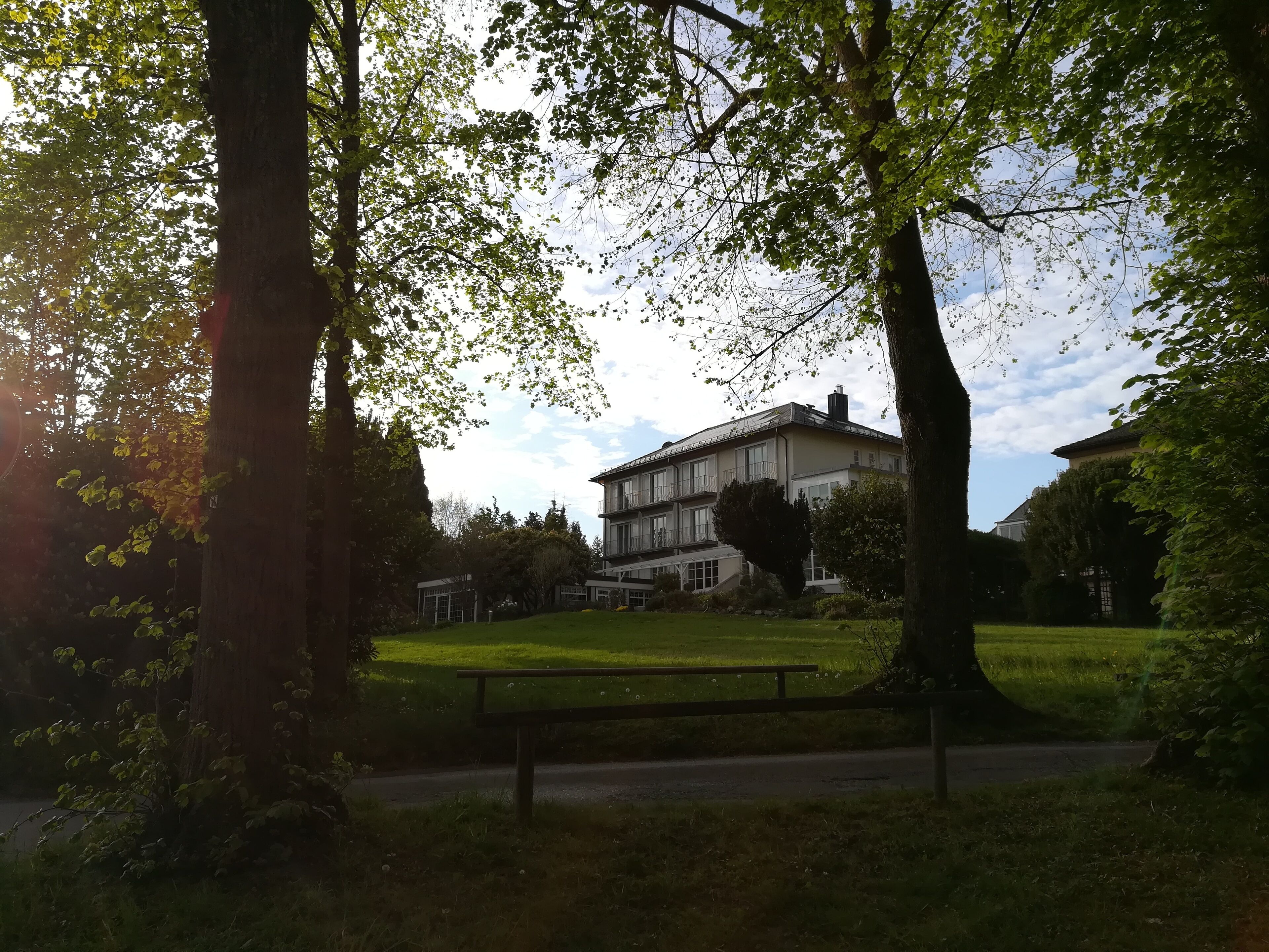 Ein großes, zweistöckiges Gebäude mit flachem Dach und zahlreichen Fenstern, umgeben von einem gepflegten Rasen und Bäumen.