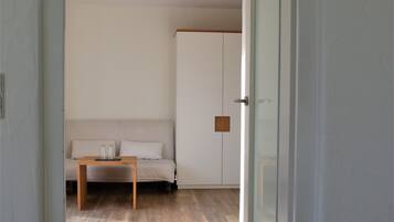 Une pièce avec un plancher en bois, un canapé blanc, une petite table et une armoire.