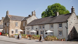 Un edificio de piedra tradicional con un letrero que dice "The Devonshire Arms" y mesas exteriores con sombrillas.