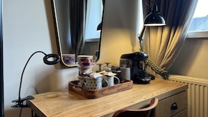 Un escritorio de madera con un espejo, una lámpara y varios objetos, incluyendo una bandeja con recipientes y una taza.