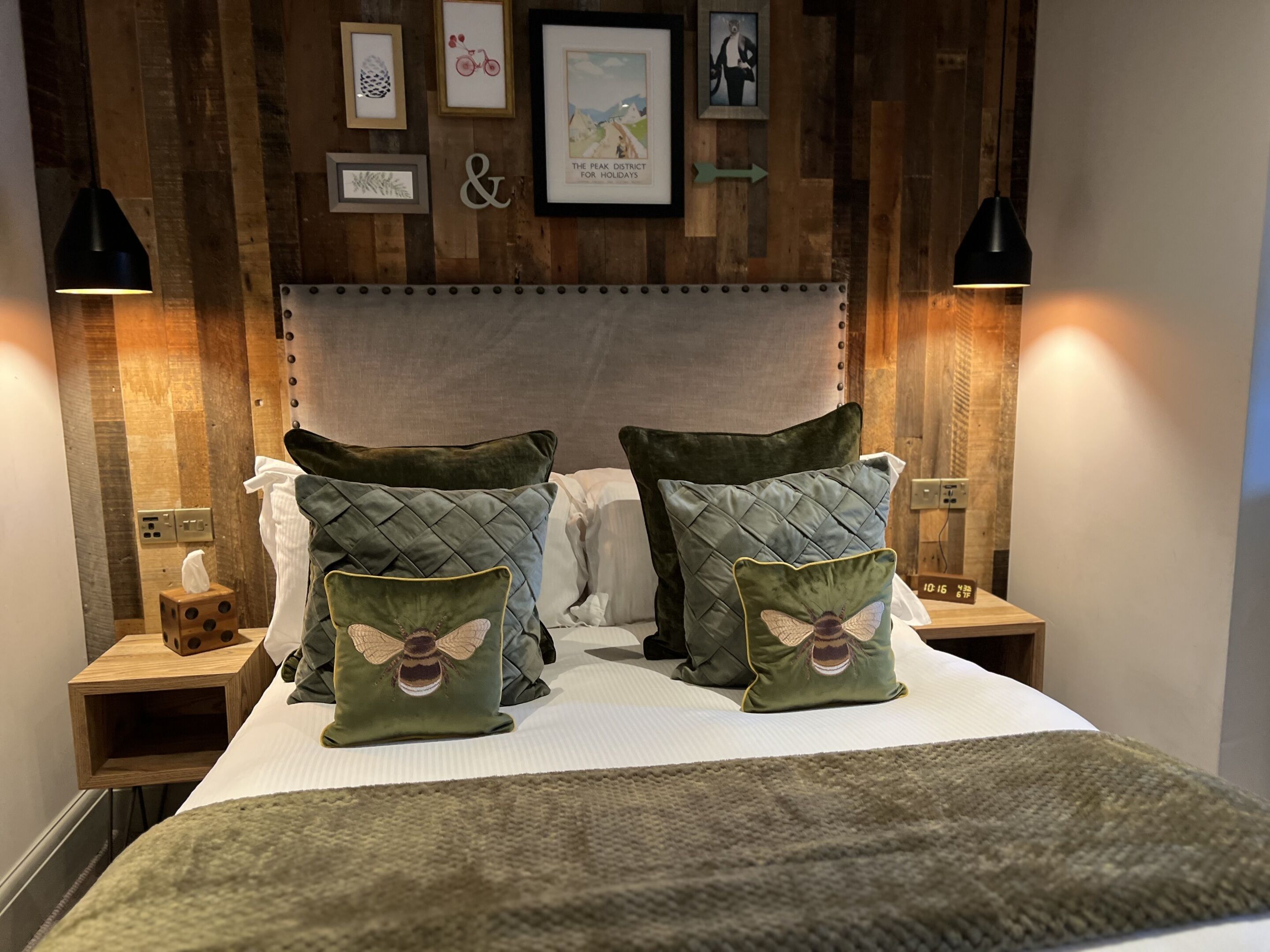 A neatly made bed with two pillows featuring a bee design, wooden paneling on the walls, and framed pictures on the wall.