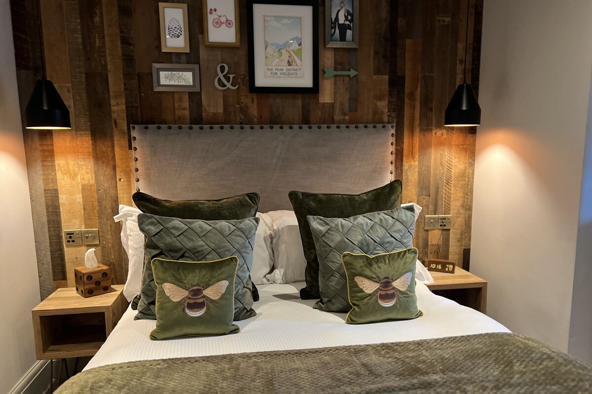 Uma cama bem arrumada com duas almofadas com estampa de abelha, painéis de madeira nas paredes e quadros decorativos.