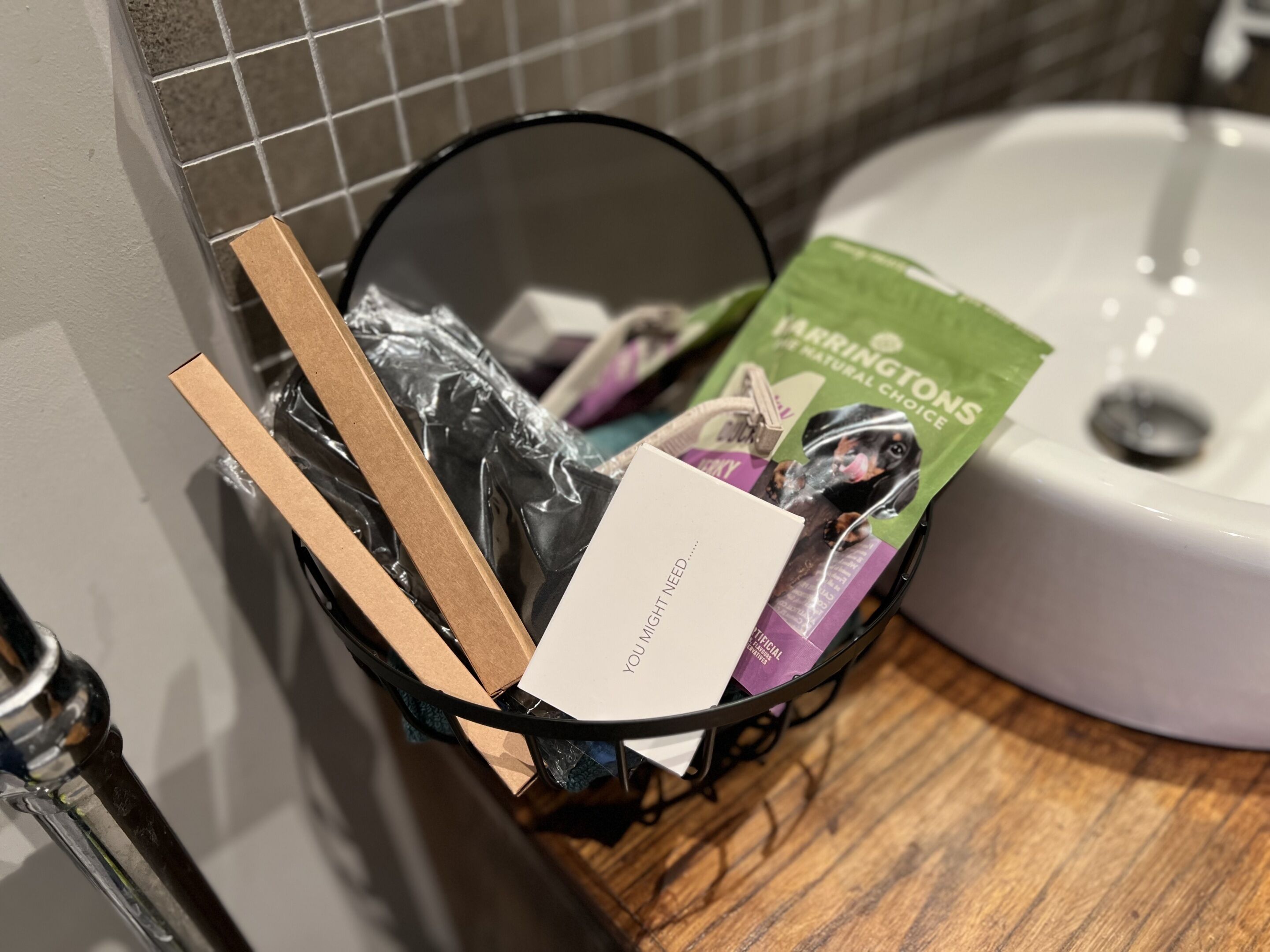 Un cestino della spazzatura con una card etichettata “POTRESTI AVER BISOGNO…” e una borsa di cibo per cani.