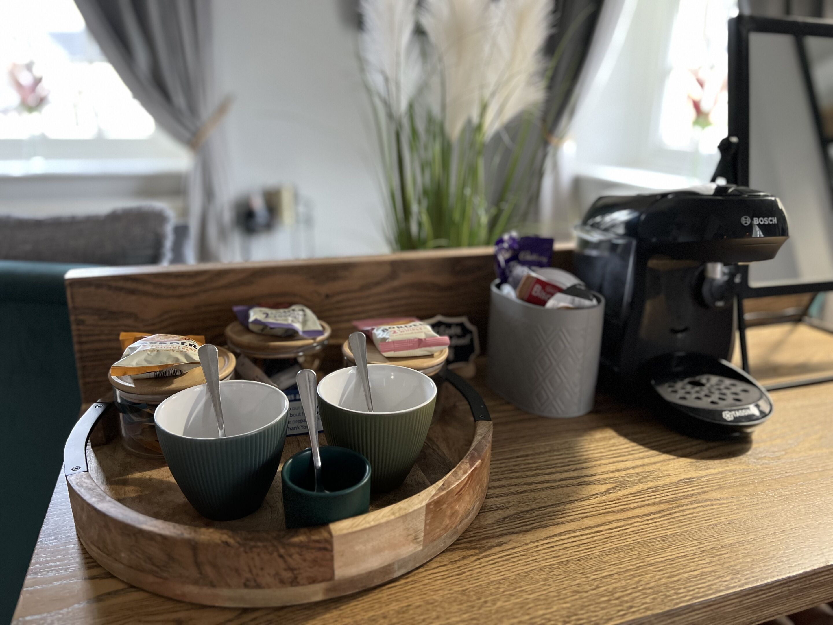 Un vassoio di legno con tazze e una macchina da caffè su un tavolo.
