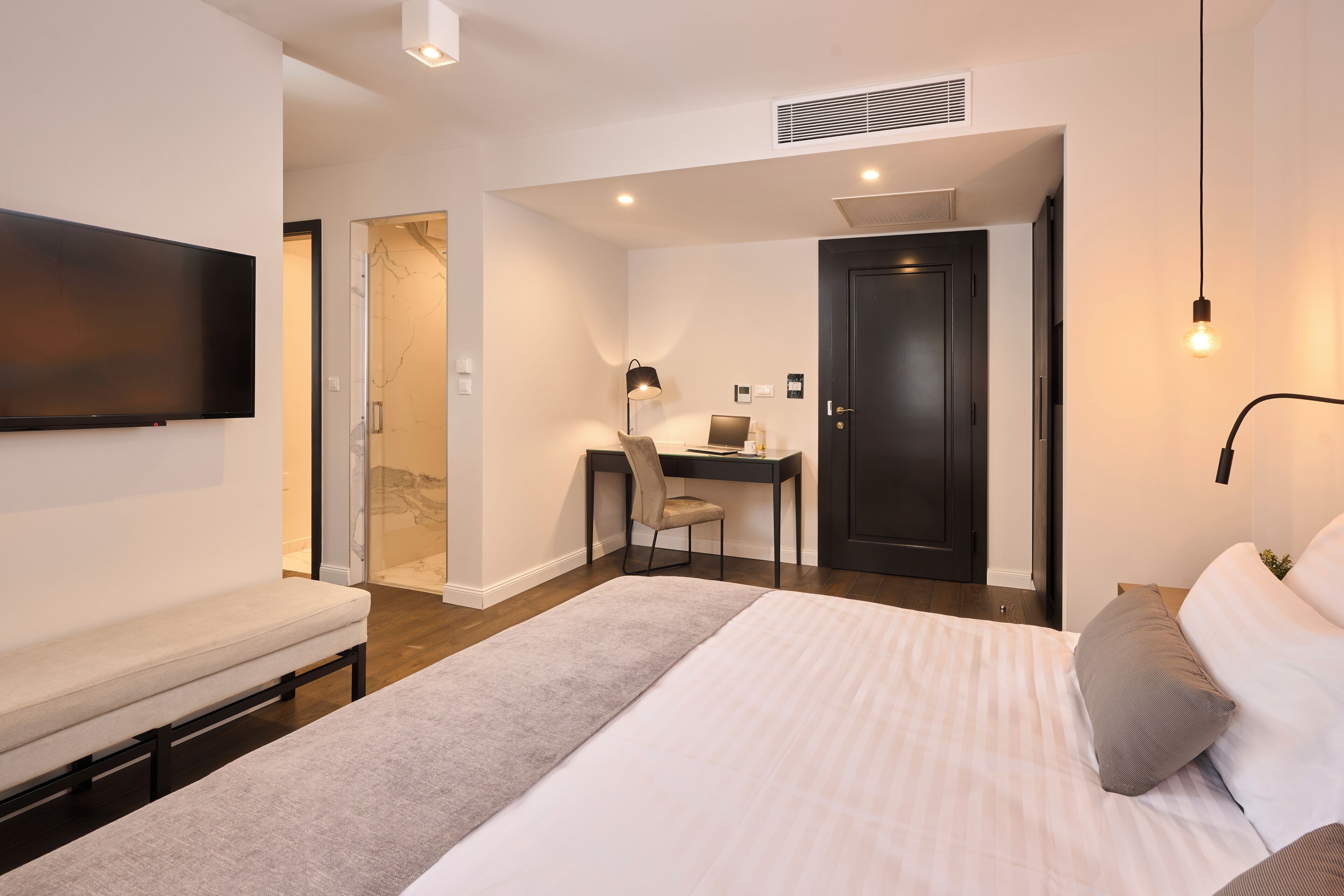A modern hotel room with a bed, a desk, a chair, a TV, and a door.