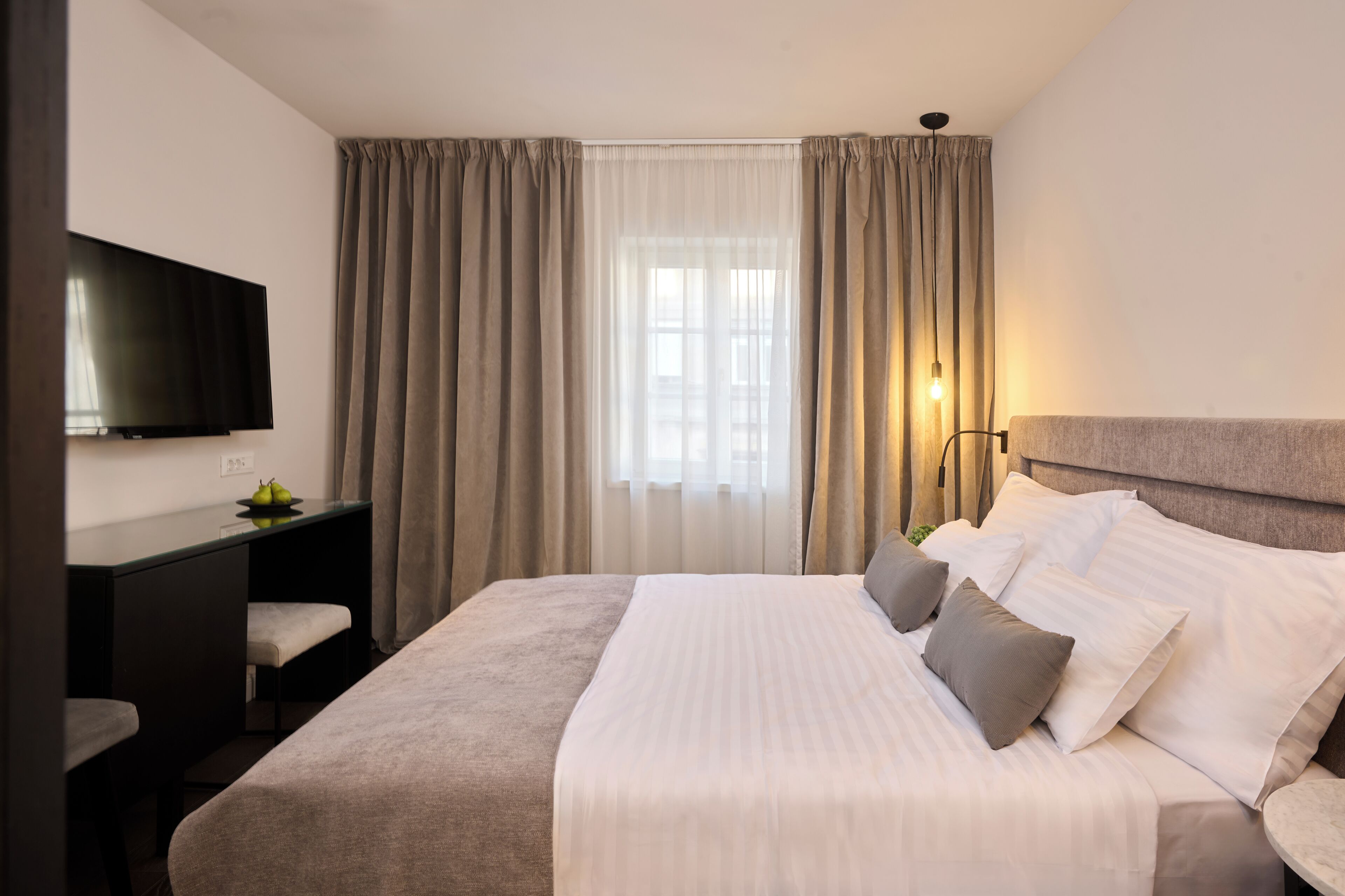 Una habitación de hotel con cama, escritorio, televisor y ventana con cortinas.