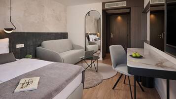 A modern hotel room with a bed, a sofa, a desk with a laptop, and a mirror.