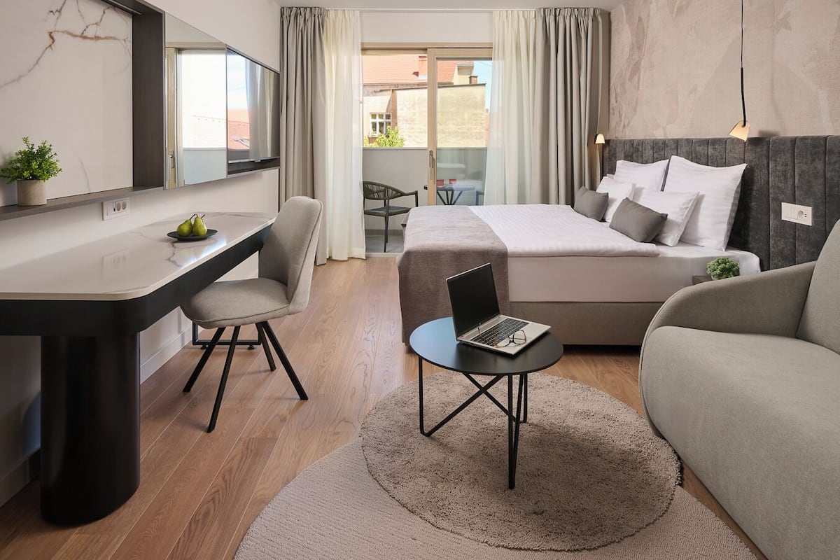 Quarto de hotel moderno com cama, escrivaninha, cadeira e sofá.