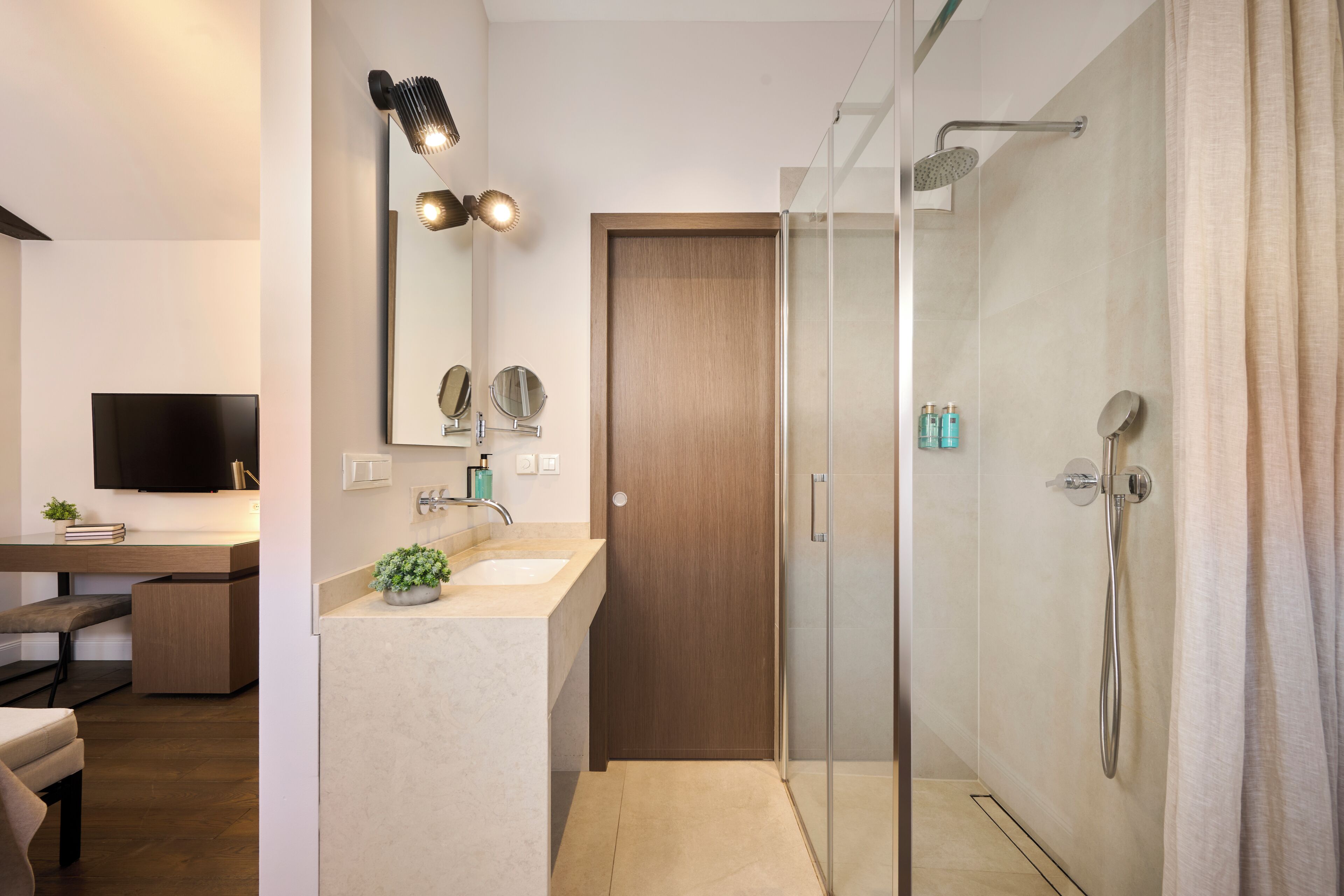 Une salle de bain moderne équipée d’une douche, d’un lavabo, d’un miroir et d’un téléviseur dans la pièce adjacente.