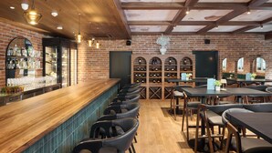 Una zona de bar con mostrador de madera, sillas de cuero negro y estanterías para vino.