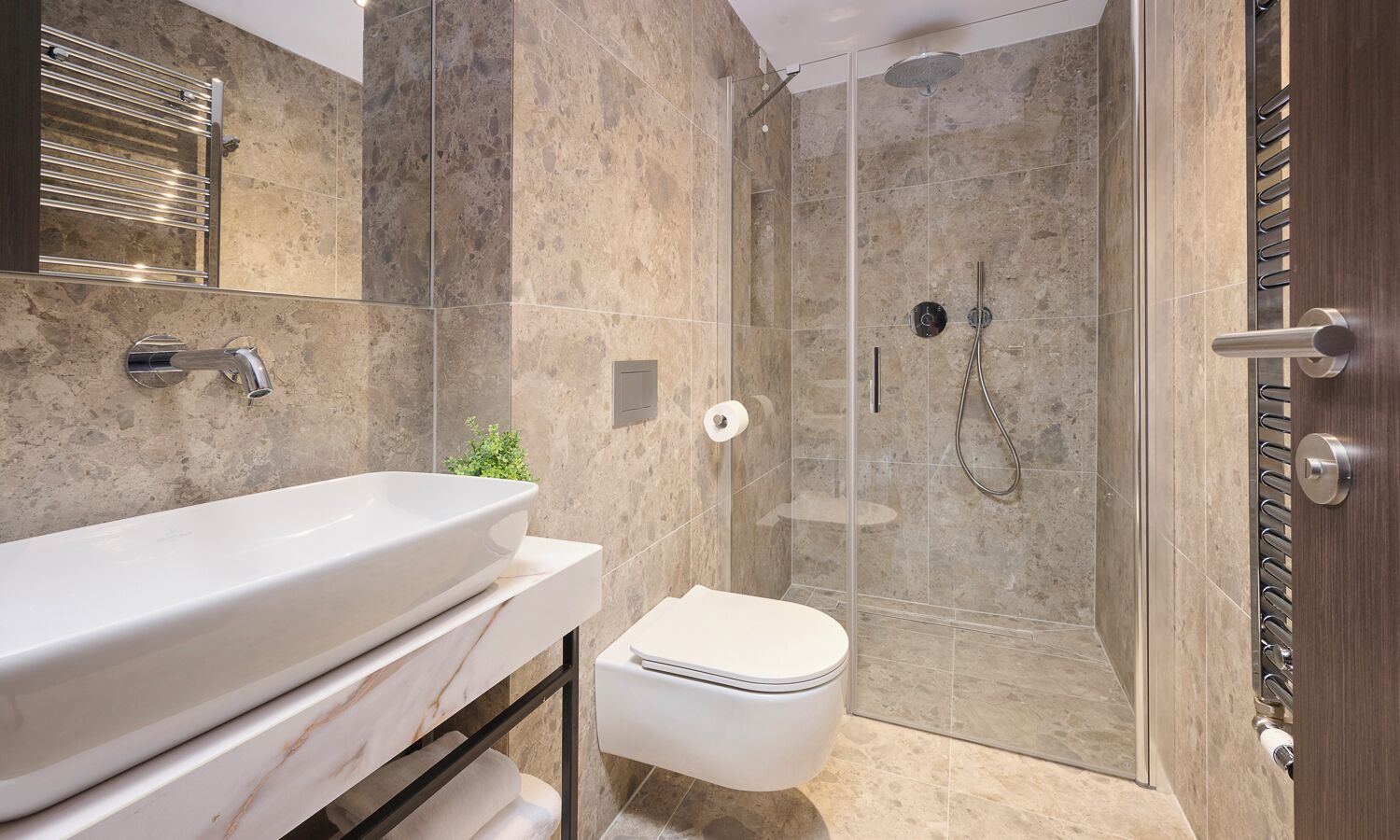 Un baño moderno con un lavamanos blanco grande, un inodoro y una zona de ducha con mampara de vidrio.