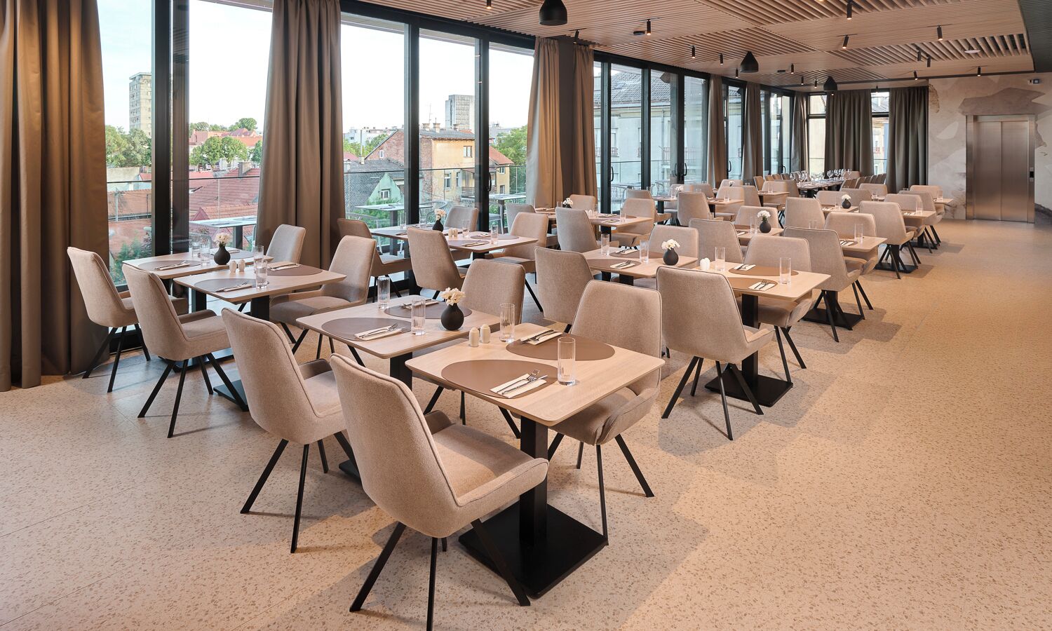 A modern dining area with tables and chairs, large windows, and an elevator.