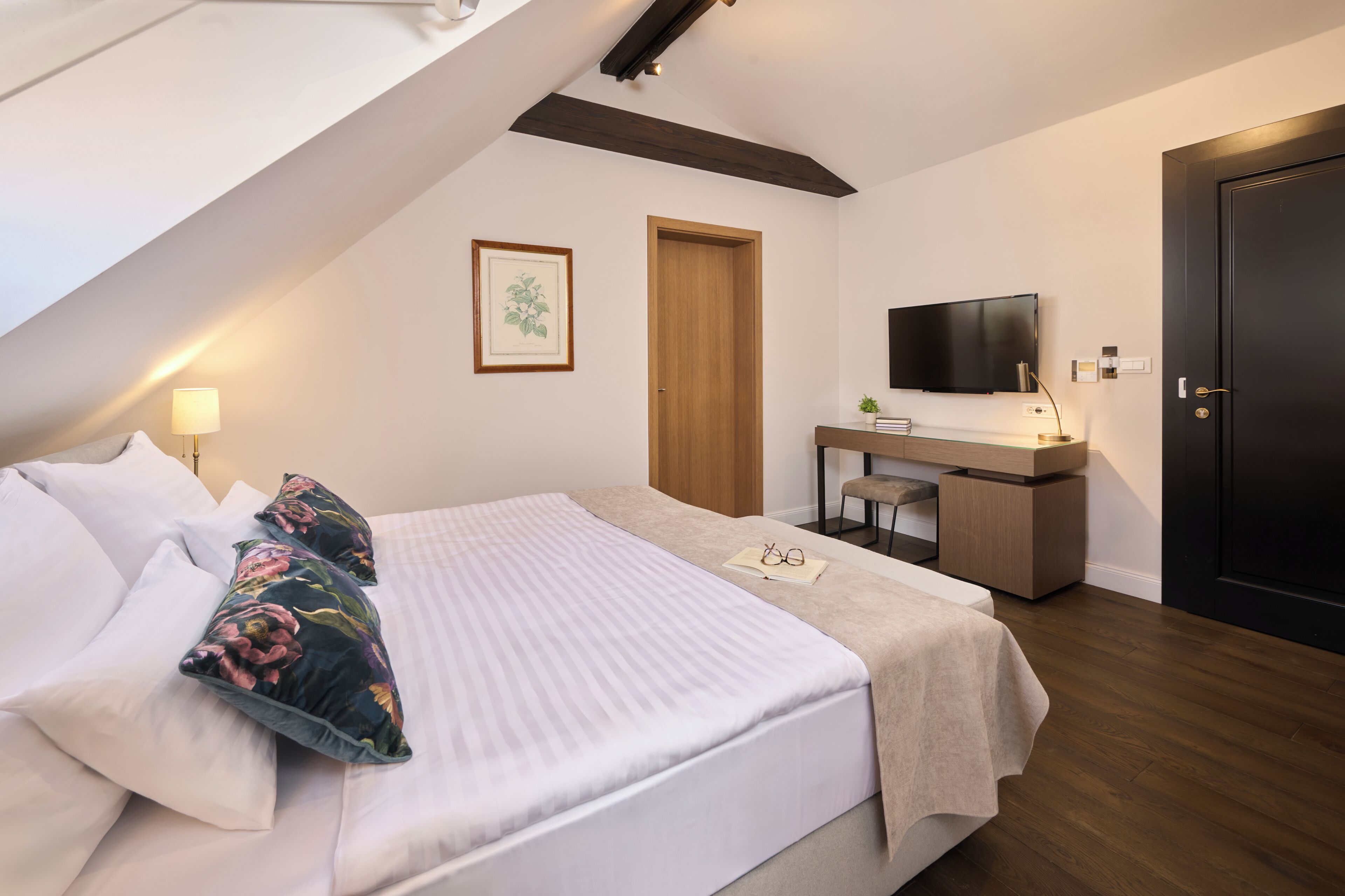 Un dormitorio con cama, mesita de noche, televisor, escritorio y una puerta.