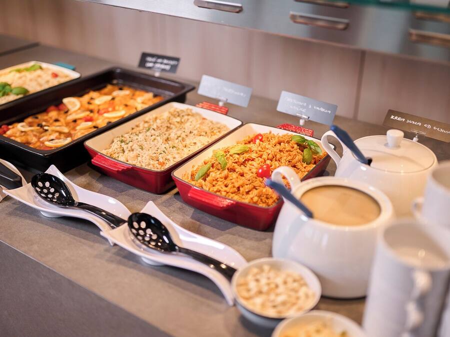 Un bufé con diversos platos, utensilios de servicio y tazas de café.