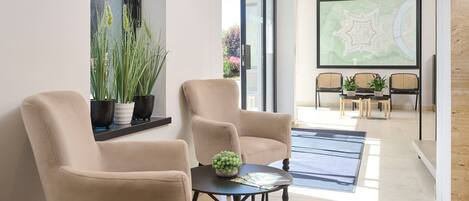Un interior moderno con dos sillones color beige, una mesita con una planta y una zona de comedor con sillas de mimbre y un mapa en la pared.