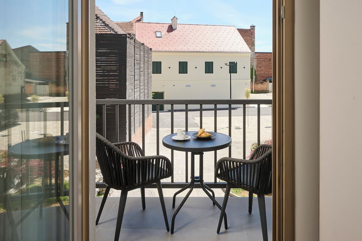Uma varanda com duas cadeiras e uma mesa, vista de um edifício com telhado vermelho e céu claro.