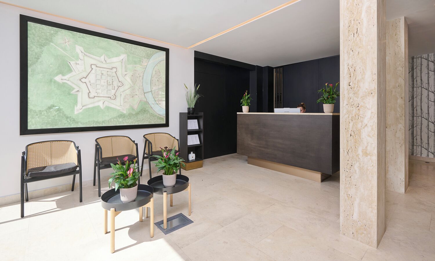 A reception area with a large map, three wicker chairs, a reception desk, and potted plants.
