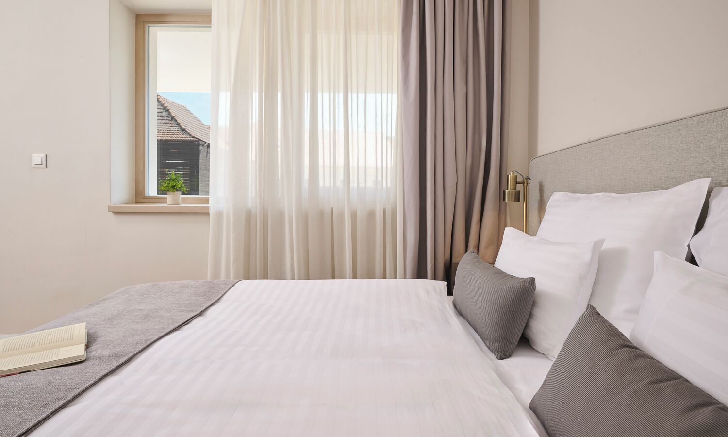 A hotel room with a bed, curtains, a window, and a bedside lamp.