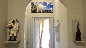 A hallway with a door leading to a bright room, a mannequin dressed in white, and a sculpture on a shelf. - Art&B.E.D.S. (Naples)