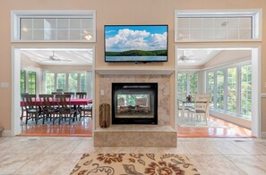 A living room with a fireplace, a television mounted above it, and a dining area with a table and chairs.