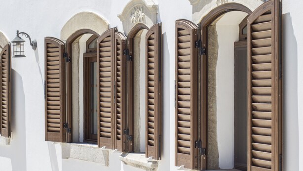 A building with multiple windows featuring wooden shutters, stone arches, and a wall-mounted lantern. - Villa Angel | 2 Bedrooms | Panoramic Views | Parragil (Loulé)