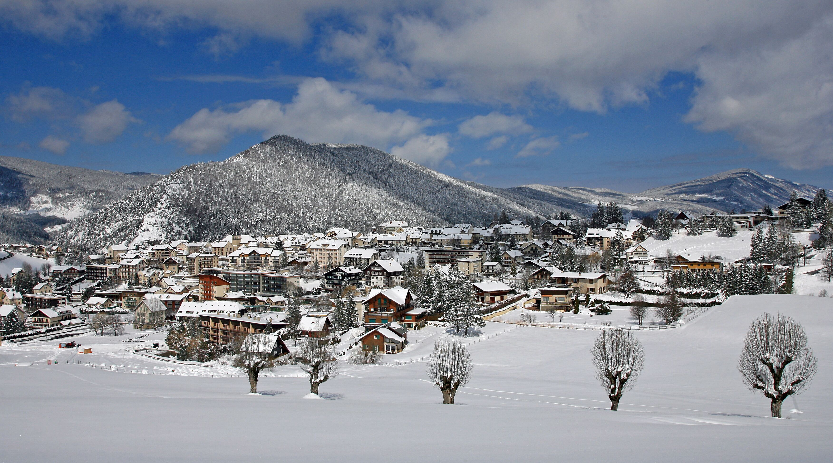 Un pueblo cubierto de nieve con edificios, árboles y montañas al fondo.
