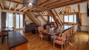 A spacious loft with a high ceiling, wooden beams, a large dining table with chairs, a sofa, and a staircase. - Residence Le Splendid (Villard-de-Lans)