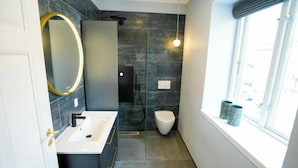 Een moderne badkamer met een wit wastafelmeubel, een grote spiegel, een douche en een raam met twee decoratieve vazen.