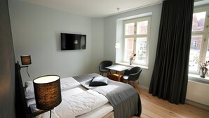 Een hotelkamer met een bed, nachtlampjes, een bureau, een stoel, een raam met gordijnen en een wandgemonteerde flatscreen-tv.