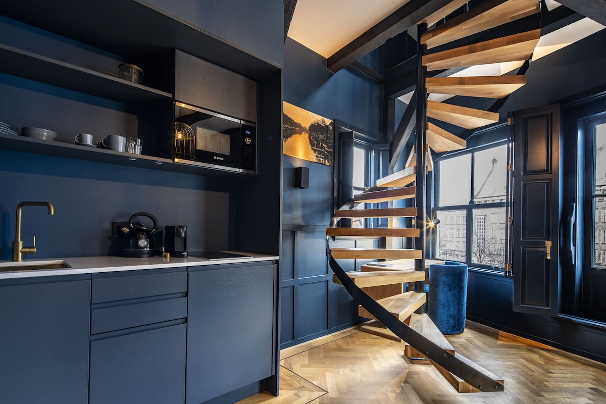 A modern kitchen with a built-in stove, a coffee machine, and a sink. There is a wooden staircase leading to an upper level.