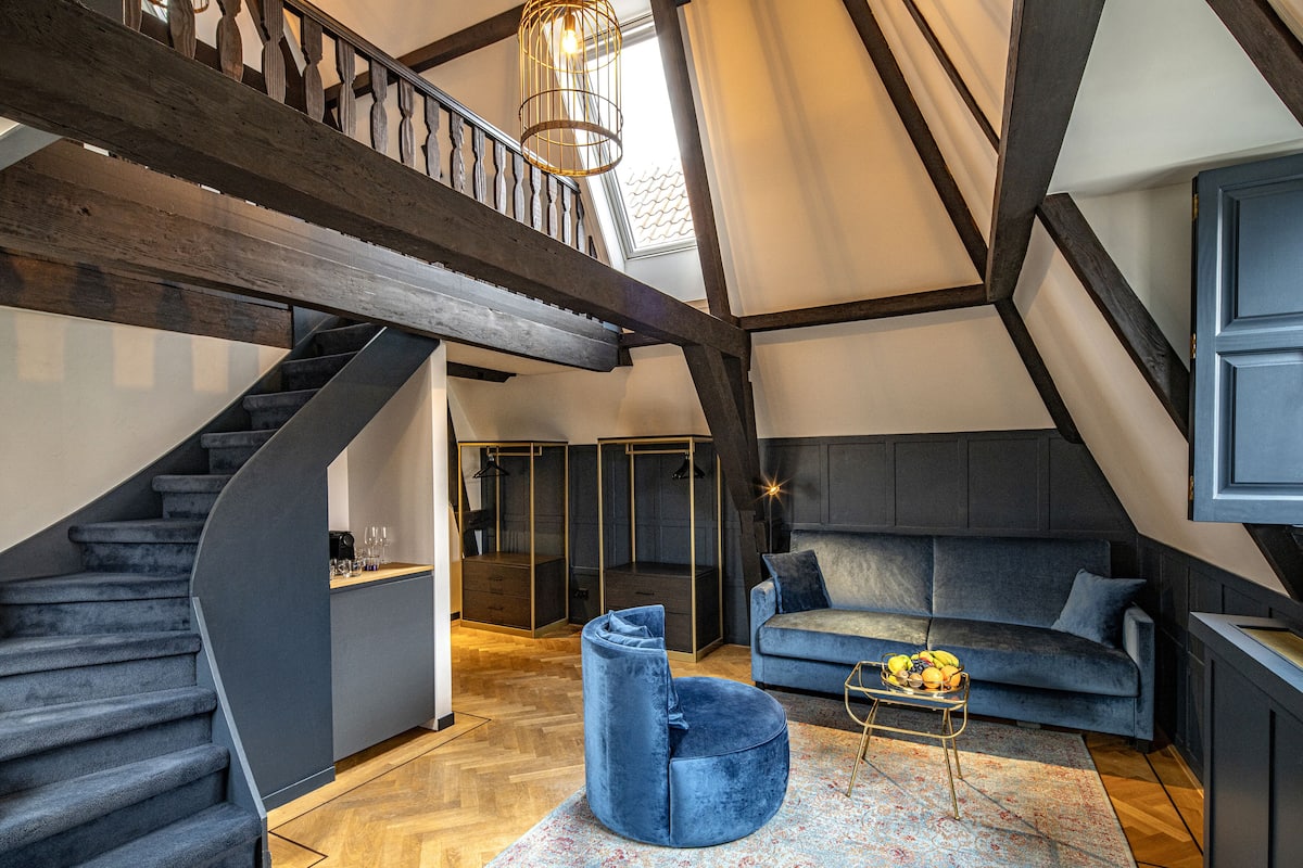 A modern loft with a spiral staircase, a blue sofa, and a dining area with a fruit bowl.