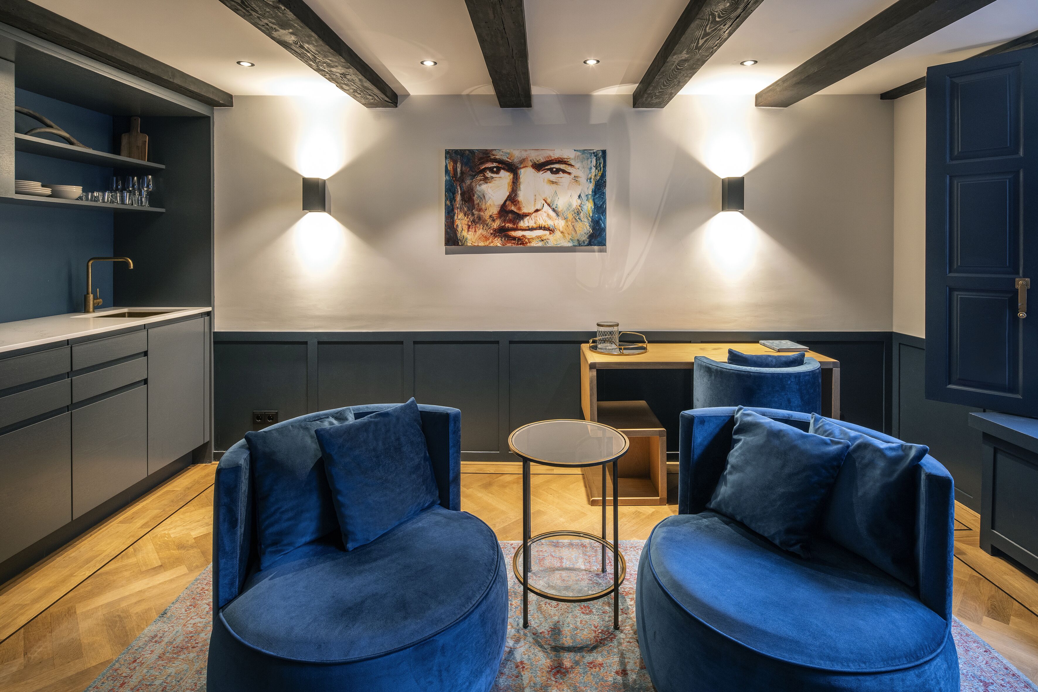 Un salon moderne avec deux canapés bleus, une petite table ronde et un tableau accroché au mur.