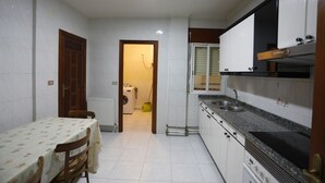 A compact kitchen with white cabinets, a granite countertop, and a dining area with a table and chairs. - Apartamento San Antonio (Monforte de Lemos)