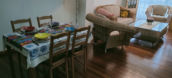Un coin repas avec une table dressée pour quatre personnes, entouré de chaises en osier et d’un canapé.