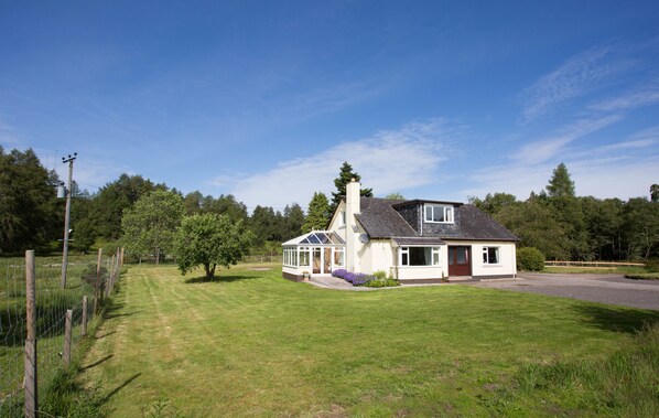 A single-story house with a covered porch, a chimney, and a well-maintained lawn. - Juniper Hill, Loch Achilty (Strathpeffer)