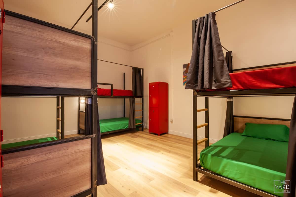 Une chambre de dortoir avec des lits superposés, une armoire rouge et une couverture verte.