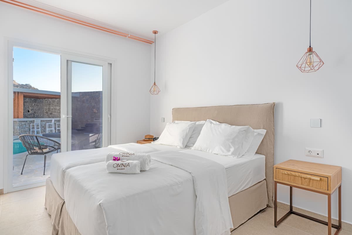 Ein Schlafzimmer mit einem Bett, einem Nachttisch, einer Hängelampe und Blick ins Freie.
