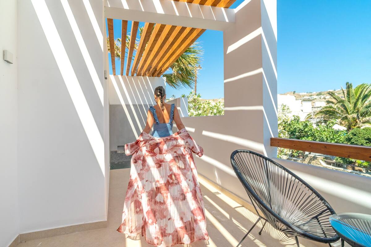 Ein Balkon mit einer Holzpergola, einem Stuhl und Blick auf Palmen und Gebäude.