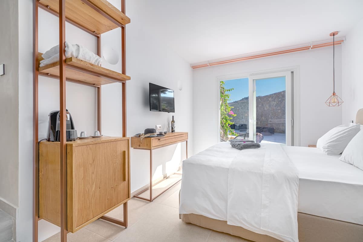 Ein modernes Schlafzimmer mit Bett, einem Holztisch, einem Fernseher und Blick ins Freie.